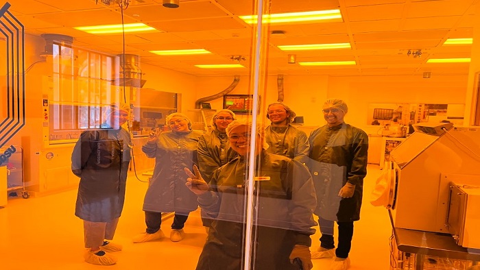 SDSU students posing in lab behind glass windows in full gown