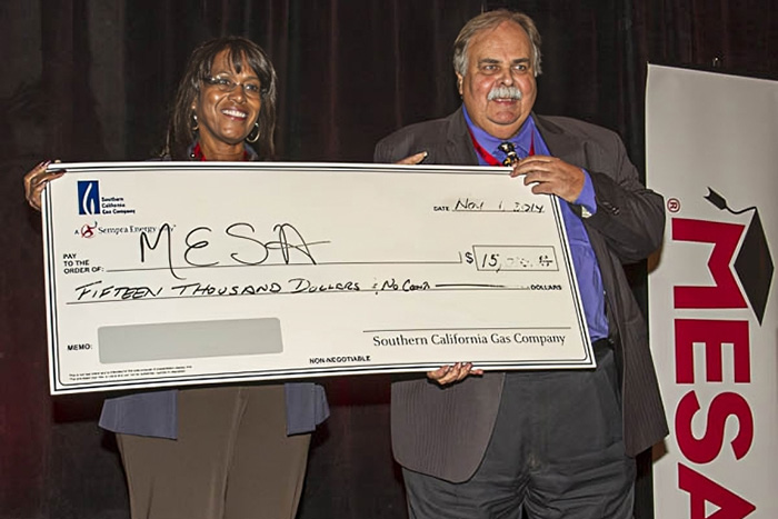 Two individuals holding an oversized promotional check between them. The check is from the Southern California Gas Company, dated Nov 1, 2017, and made out for fifteen thousand dollars to 'MESA,' which stands for Mathematics, Engineering, Science Achievement.